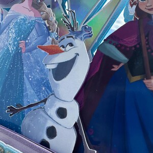 May include: A layered image featuring characters from the animated film "Frozen." Olaf the snowman is in the foreground, with Elsa and Anna in the background. The image has a glittery, iridescent finish with shades of blue, purple, and silver.