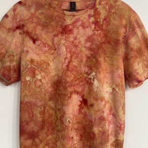 May include: A short-sleeved t-shirt with a tie-dye pattern in shades of red, orange, and yellow. The shirt is hanging on a wooden hanger against a white background. The tie-dye design creates a unique, artistic look.