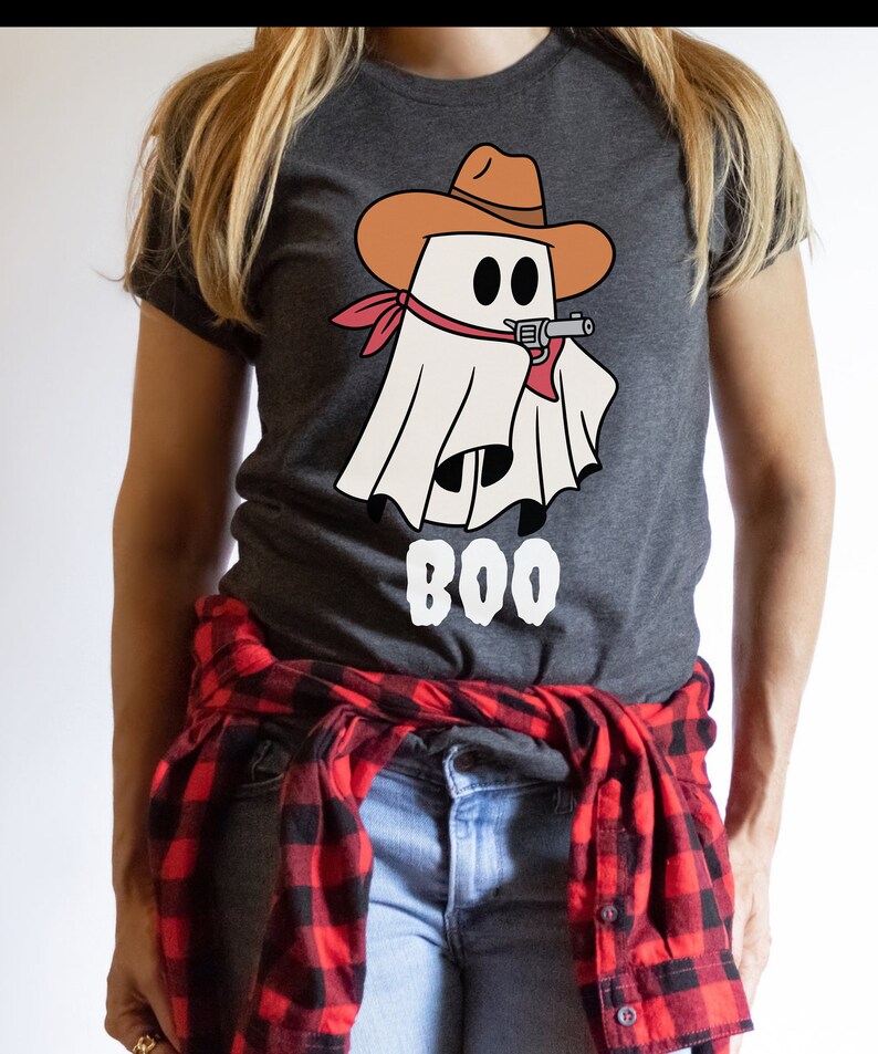 Może przedstawiać: Szary t-shirt z białym duchem w brązowym kowbojskim kapeluszu trzymającym pistolet. Duch ma czerwoną chustkę na szyi. Pod duchem nadrukowany jest napis "BOO".