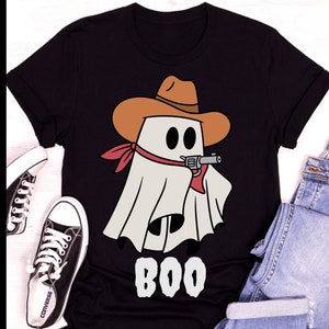 Może przedstawiać: Czarny T-shirt z białym duchem w brązowym kowbojskim kapeluszu i czerwonej chustce trzymającym pistolet. Duch m&oacute;wi "BOO" białymi literami.