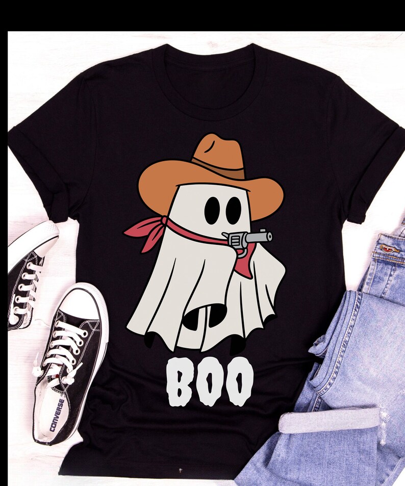 Może przedstawiać: Czarny T-shirt z białym duchem w brązowym kowbojskim kapeluszu i czerwonej chustce trzymającym pistolet. Duch m&oacute;wi "BOO" białymi literami.