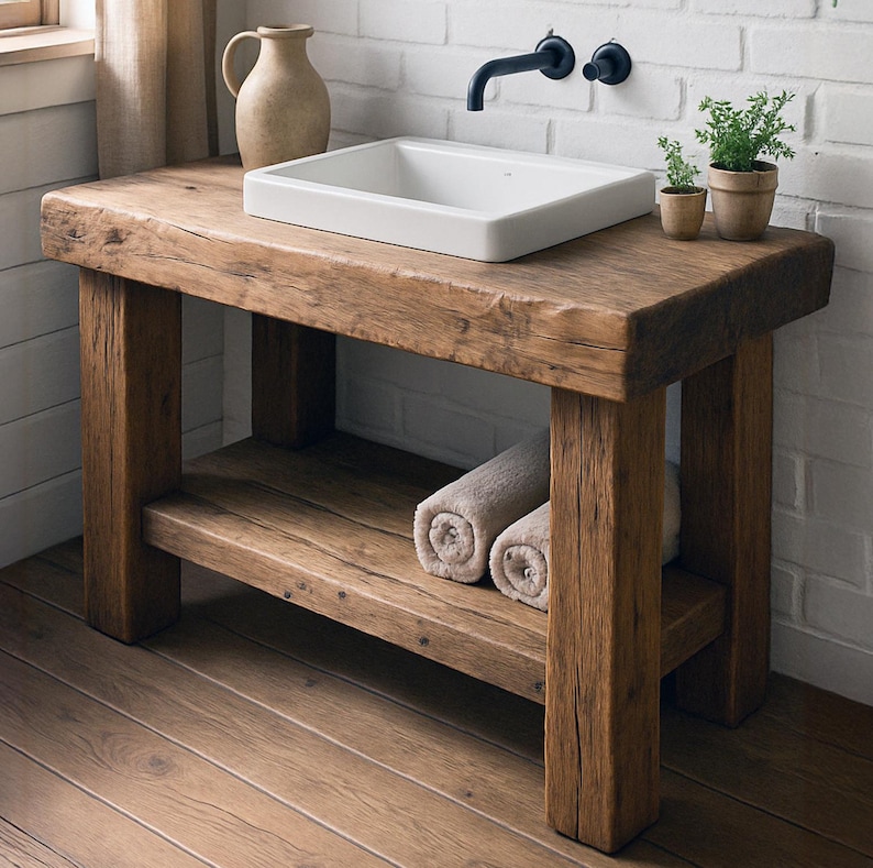 May include: A rustic wooden bathroom vanity with a white rectangular sink. The vanity has a lower shelf with rolled towels. A black faucet and small potted plants sit on the wooden surface. The wood has a natural, weathered appearance.
