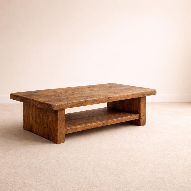May include: A rectangular coffee table crafted from weathered brown wood, featuring a thick solid top and a lower shelf supported by two sturdy block legs on each side, showcasing a natural grain and a textured, rustic finish throughout.