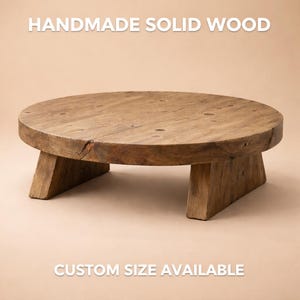 May include: A handmade, solid wood, round table with three angled legs. The table is a natural wood colour with visible grain and knots. The text "CUSTOM SIZE AVAILABLE" is at the bottom of the image.