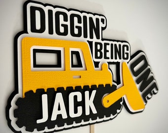 May include: Yellow and black construction vehicle cutout with the text "Diggin' Being One Jack" on the front. The vehicle has a shovel attached to the side.
