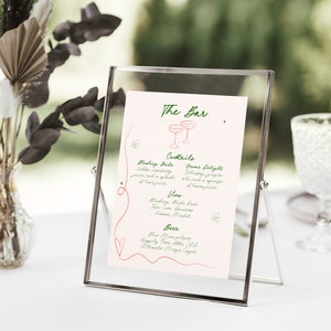 Pu&ograve; includere: Un cartello rosa e bianco con testo verde in una cornice argentata. Il cartello recita "The Bar" e elenca le opzioni di cocktail, vino e birra. Il cartello &egrave; su un tavolo bianco con un vaso di fiori secchi.