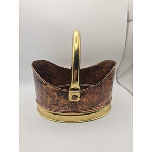 Peut inclure: Un panier de forme ovale doté d'un corps en cuivre martelé avec une finition patinée tachetée. Le panier comprend une poignée en laiton poli fixée par des rivets et un bord de base en laiton lisse, contrastant avec la surface en cuivre texturée.