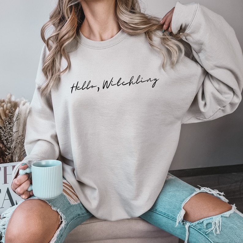 May include: A light gray sweatshirt with the text "Hello, Witchling" in black script.