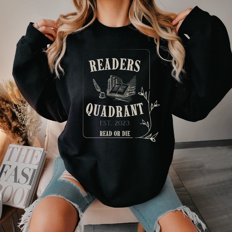 May include: Black sweatshirt with a white graphic design that says "Readers Quadrant Est. 2023 Read or Die". The graphic features a quill pen, an open book, and a stack of books.