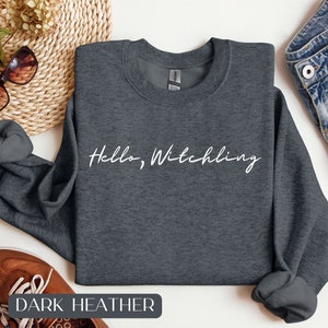 May include: Dark heather grey sweatshirt with the text "Hello, Witchling" in white cursive lettering.