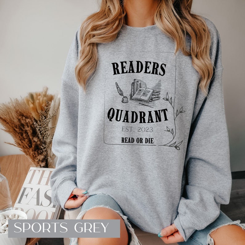 May include: A grey sweatshirt with a black graphic design that says "Readers Quadrant Est. 2023 Read or Die". The graphic features a quill pen, an open book, and a stack of books.