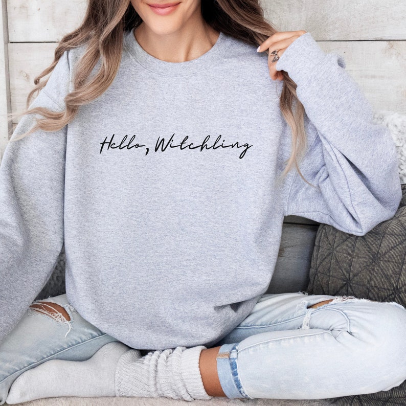 May include: A gray sweatshirt with the text "Hello, Witchling" in black script.