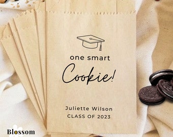 Könnte beinhalten: Ein Stapel brauner Papiertüten mit einem Abschluss-Hut-Design und dem Text "one smart Cookie!"  Juliette Wilson CLASS OF 2023.