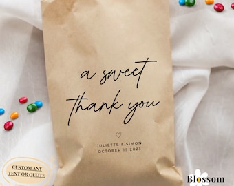 May include: A brown paper bag with the text "a sweet thank you" and a heart symbol. Below the text is "Juliette & Simon October 15 2023". The bag is on a white surface with colorful candies scattered around it.