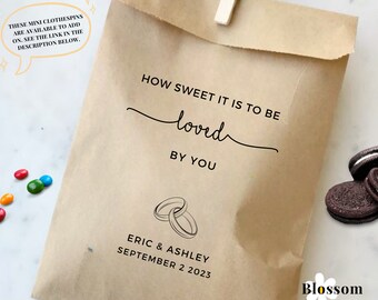 May include: A brown paper bag with the text "How sweet it is to be loved by you" and a drawing of two wedding rings. The bag also has the text "Eric & Ashley September 2 2023" and a logo that says "Blossom Paperie Shop".