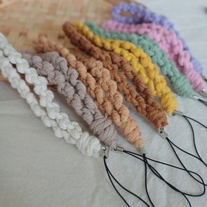 May include: A set of six colorful phone straps made of braided cotton cord. The straps are in various shades of brown, yellow, green, pink, and purple. Each strap has a black cord loop and a silver metal clasp.
