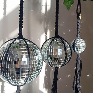 Può includere: Tre ornamenti a forma di palla da discoteca appesi a corde nere con nappe. Le palle da discoteca sono di dimensioni diverse e sono fatte di piastrelle a specchio.