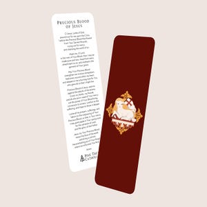 May include: Two bookmarks. One white with text, the other burgundy with a gold emblem. The white bookmark has the text "PRECIOUS BLOOD OF JESUS". The burgundy bookmark features a lamb with a cross and a decorative gold border. Religious themed.