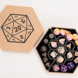 May include: A hexagonal box with a lid, the lid has a printed image of a 20-sided die. The box is open and contains a set of dice in various colors and designs, including brown, pink, and purple.