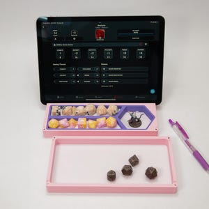 May include: A pink and purple dice tray with a miniature figure and dice. The tray is divided into sections for different types of dice. A tablet with a digital character sheet is in the background.