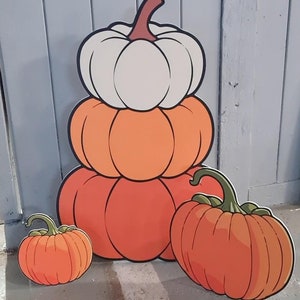May include: A stack of four pumpkins, one white, two orange, and one small orange pumpkin. The pumpkins are stacked on top of each other, with the white pumpkin on top. The pumpkins are all cartoon-style and have a simple design.
