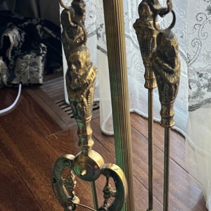 Puede incluir: Un juego de herramientas para chimenea de metal dorado con un soporte decorativo. El juego incluye un cepillo, una pala y un atizador.