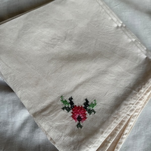 May include: A white linen napkin with a red and green embroidered flower design.