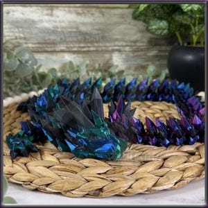 May include: A black, green and purple iridescent dragon sculpture made of crystal-like pieces. The dragon is lying on a woven straw mat.