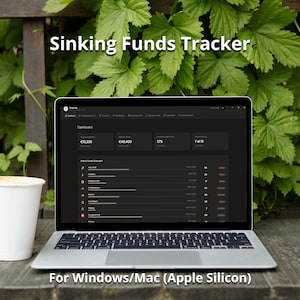May include: A laptop displaying a "Sinking Funds Tracker" dashboard with financial data. The screen shows figures in Euros, percentages, and a list of active funds. The laptop is on a wooden surface with a white cup and green foliage in the background.