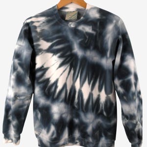 May include: A crew neck sweatshirt with a tie-dye pattern in shades of black and white. The long-sleeved top is hanging on a wooden hanger. The tie-dye design has a spiral effect.