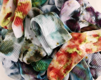 May include: A pile of colorful, tie-dye socks. The socks are a mix of white, blue, green, yellow, red, and purple. The socks are made of a ribbed knit material.