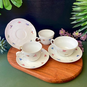 May include: A set of three white porcelain teacups and saucers with a floral pattern. The cups and saucers have a delicate floral design in shades of pink, blue, and yellow.
