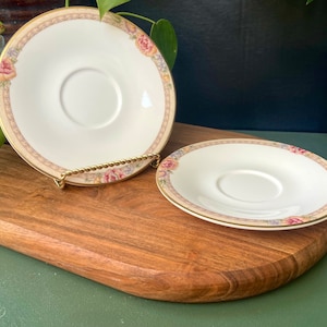May include: Two white porcelain teacups with floral patterns and gold trim. The cups are on a wooden surface.