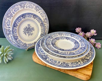 May include: Set of four blue and white ceramic plates with a floral pattern. The plates are nested together and are on a wooden cutting board.