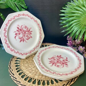 May include: Three white octagonal ceramic dinner plates with a pink floral design. The plates have a pink floral pattern with a border of pink leaves.