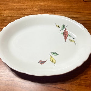 May include: White oval serving dish with a scalloped edge and a design of green, pink, and yellow leaves.