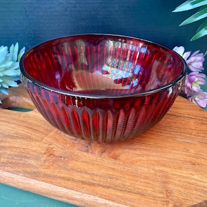 May include: A deep red glass bowl with a ribbed design. The bowl is sitting on a wooden cutting board.