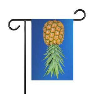 May include: A garden flag with a blue background featuring a pineapple with a yellow and brown fruit and green leaves.