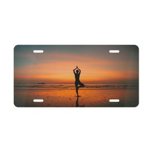 May include: Silhouette of a person doing yoga on a beach at sunset. The sky is a vibrant orange and pink.
