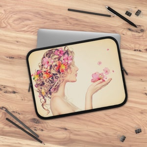 May include: A laptop sleeve with a floral design. A woman with curly blonde hair is wearing a crown of pink and orange flowers. She is holding a pink flower in her hand. The background is a light beige color.