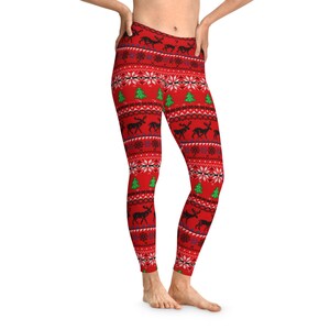 May include: Red leggings with a festive pattern featuring black reindeer, green Christmas trees, and white snowflakes. The leggings have a traditional holiday sweater design, perfect for the Christmas season.