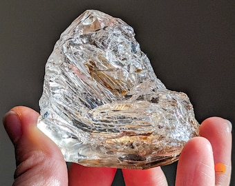 May include: A large, clear quartz crystal with a golden hue. The crystal has many facets and is shaped like a mountain.