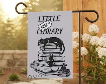 Könnte beinhalten: Eine graue Gartenflagge mit einer schwarzen Katze, die auf einem Stapel Bücher schläft. Die Flagge trägt die Aufschrift "Little Free Library" mit einem Schild, auf dem "Free" steht. Die Flagge hat auch ein Schild mit der Aufschrift "Take One Leave One" und Pfotenabdrücke am unteren Rand.