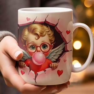 May include: White ceramic mug with a cartoon cupid design. The cupid has blonde hair, red glasses, and wings, blowing a pink bubble. The design includes hearts and a cracked wall effect, ideal for a romantic gift.
