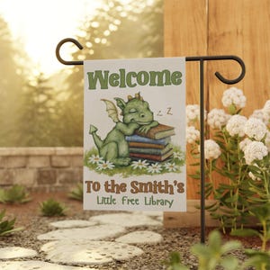 May include: A green dragon with wings is sleeping on a stack of books. The sign says "Welcome to the Smith's Little Free Library".