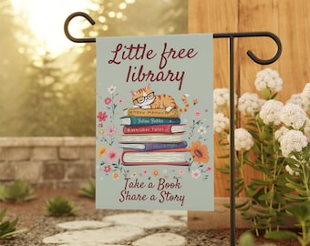 Könnte beinhalten: Eine grüne Gartenflagge mit einer Katze, die eine Brille trägt und auf einem Stapel Bücher sitzt. Die Flagge trägt die Aufschrift "Little Free Library" und "Take a Book Share a Story".