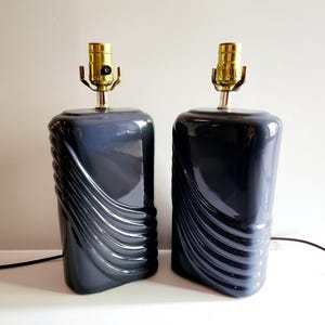 May include: A pair of dark gray ceramic table lamps with a wavy design. The lamps have brass accents and a simple on/off switch.