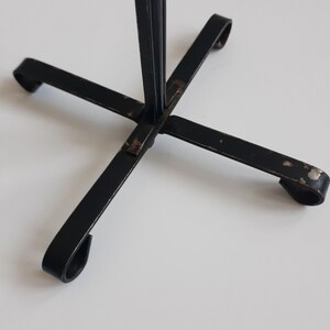 May include: Black metal stand with four legs and a single upright post. The stand has a simple, minimalist design.