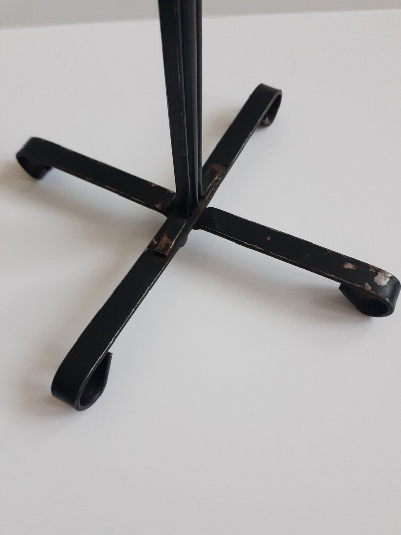 May include: Black metal stand with four legs and a single upright post. The stand has a simple, minimalist design.