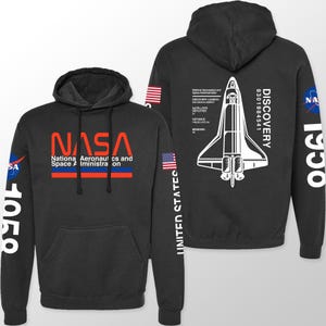 May include: Black hooded sweatshirt featuring NASA's logo in red and white, with the words "National Aeronautics and Space Administration." The back displays a white graphic of the Space Shuttle Discovery and text. The sleeves have the American flag and the number "1990".
